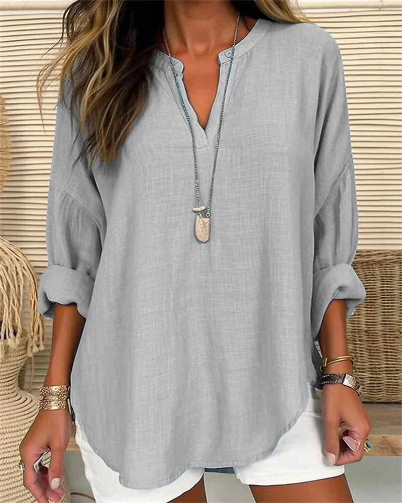 Blouse en lin gris clair pour femme, manches longues retroussées, col en V, portée avec un collier pendentif, style décontracté et élégant.
