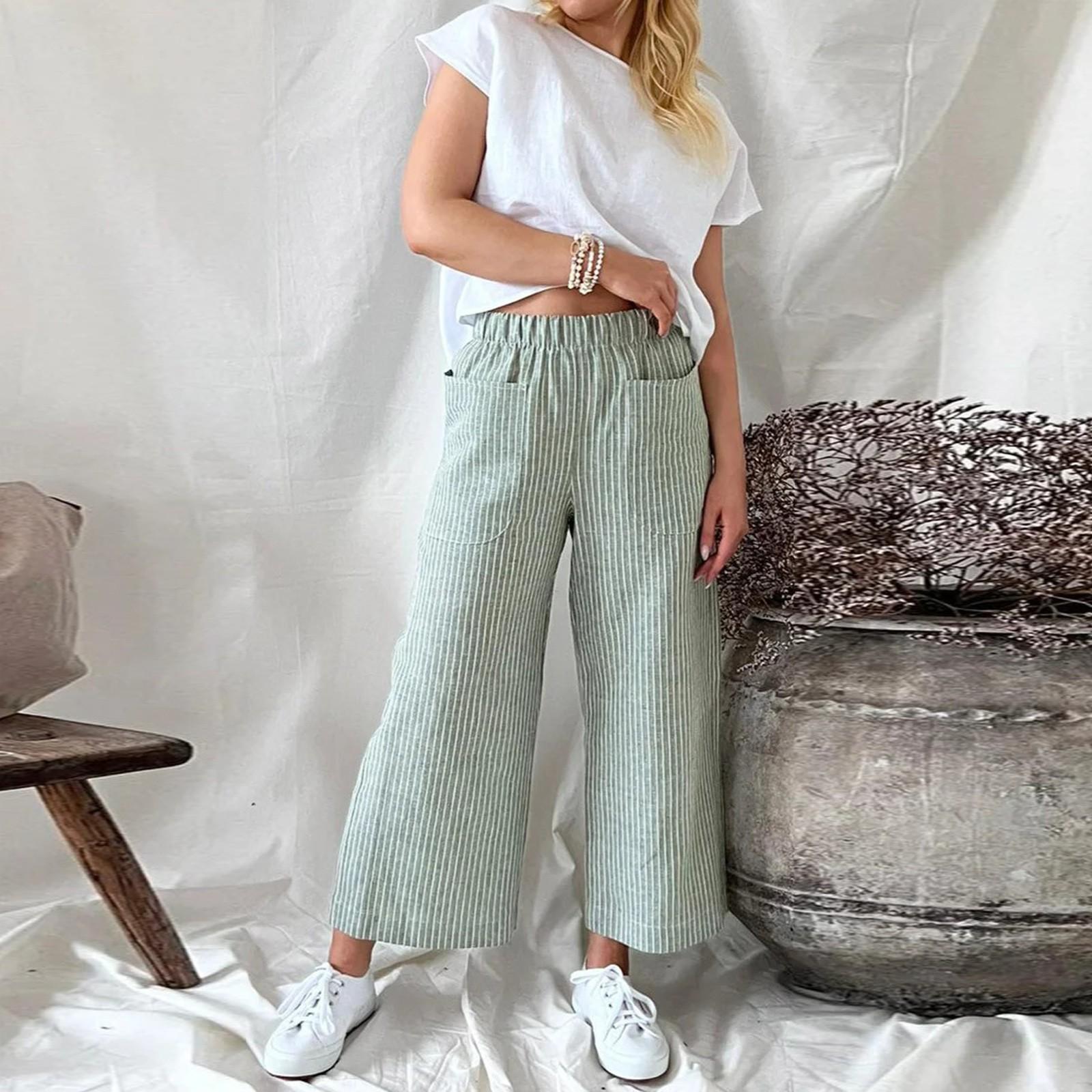 Femme en pantalon large rayé vert, t-shirt blanc, posant près d'un pot en céramique, style décontracté, mode tendance, intérieur minimaliste.