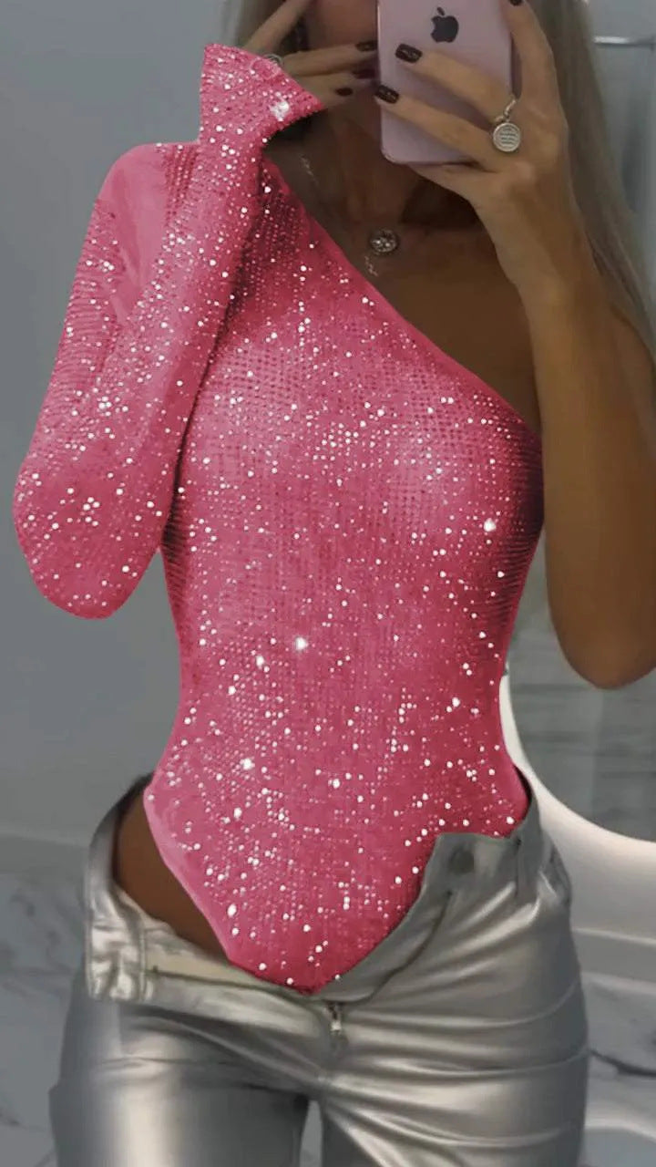 Femme portant un body asymétrique rose à paillettes, tenant un smartphone, avec un pantalon argenté. Mode tendance, tenue de soirée glamour.