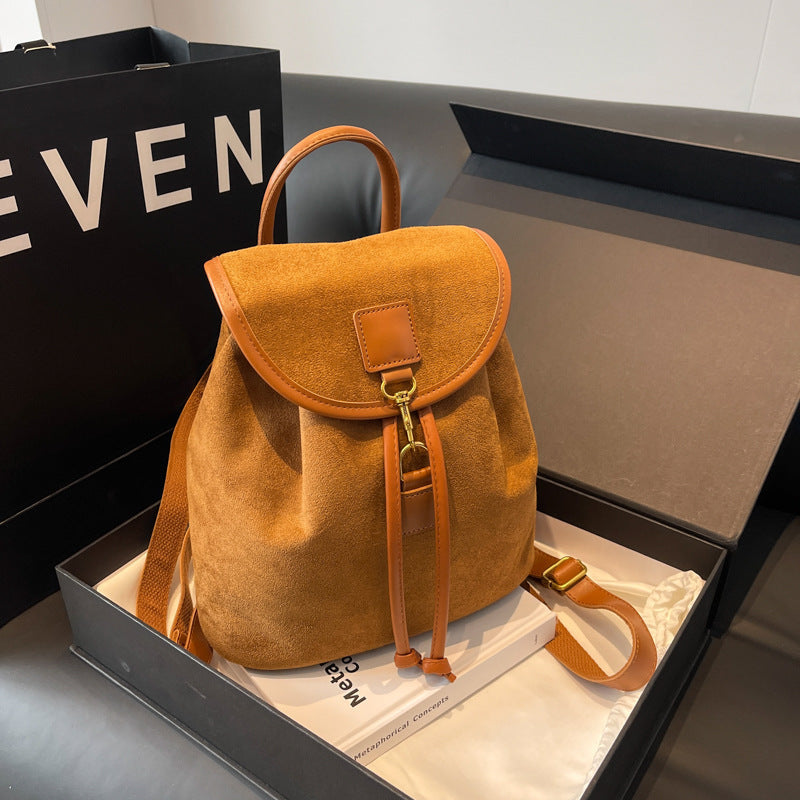 Sac à dos en daim marron avec détails en cuir, posé dans une boîte cadeau. Accessoire mode élégant, parfait pour un style urbain et tendance.