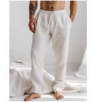 Homme portant un pantalon de détente blanc en lin, debout dans une chambre lumineuse. Mode masculine, confort, style décontracté.