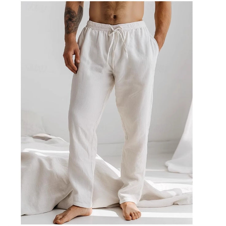 Homme portant un pantalon de détente blanc en lin, debout dans une chambre lumineuse. Mode masculine, confort, style décontracté.
