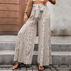 Pantalon large bohème à motifs floraux beige, ceinture nouée, femme posant devant porte en bois, style décontracté chic, mode estivale.