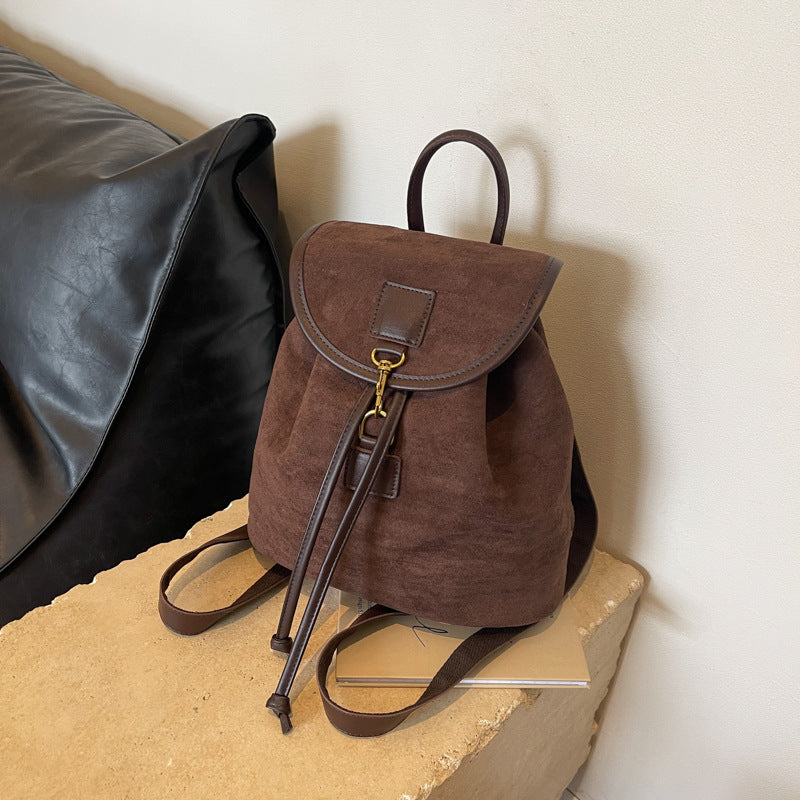 Sac à dos en toile marron avec détails en cuir, posé sur un canapé en cuir noir. Design élégant et pratique, idéal pour la mode urbaine.