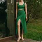 Femme en ensemble vert élégant, jupe fendue et top court, posant sur une terrasse en bois, nature en arrière-plan. Mode estivale chic.