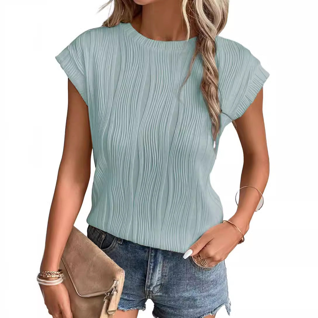 Femme portant un haut plissé bleu clair et un short en jean, tenant une pochette beige. Mode estivale, tenue décontractée, style moderne.