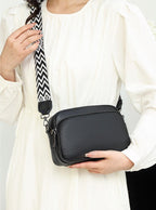 Sac à main noir en cuir texturé avec bandoulière à motif géométrique, porté par une femme en robe blanche. Accessoire mode élégant et tendance.