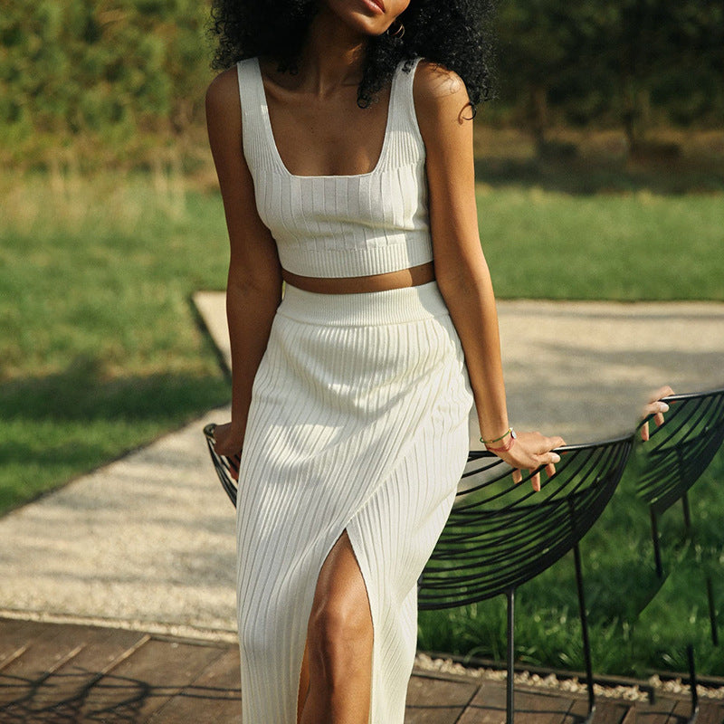 Femme en robe blanche élégante avec fente, posant dans un jardin verdoyant. Mode estivale, tenue chic, style décontracté.