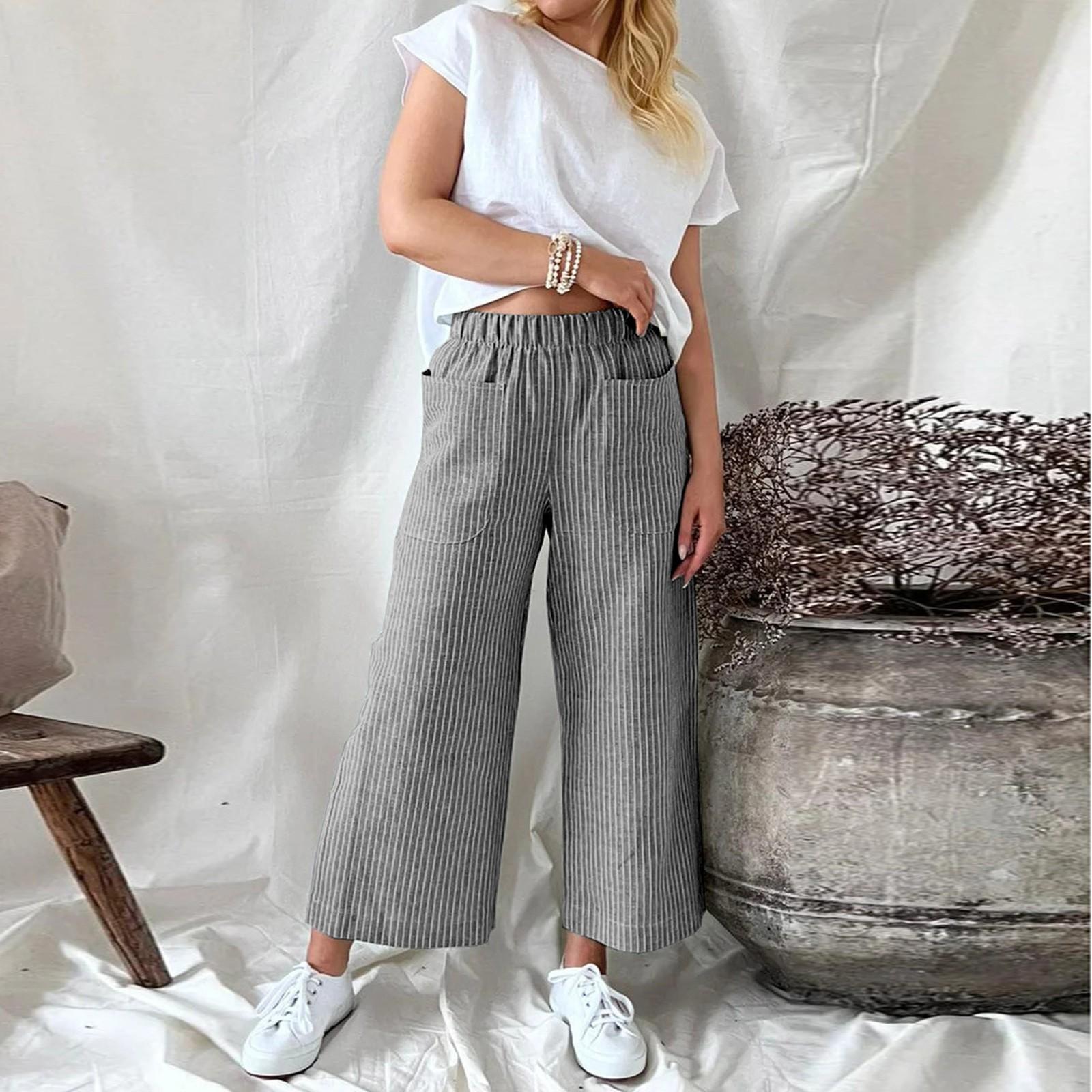 Femme en t-shirt blanc et pantalon large rayé gris, posant près d'un grand vase en terre cuite, style décontracté, mode contemporaine.