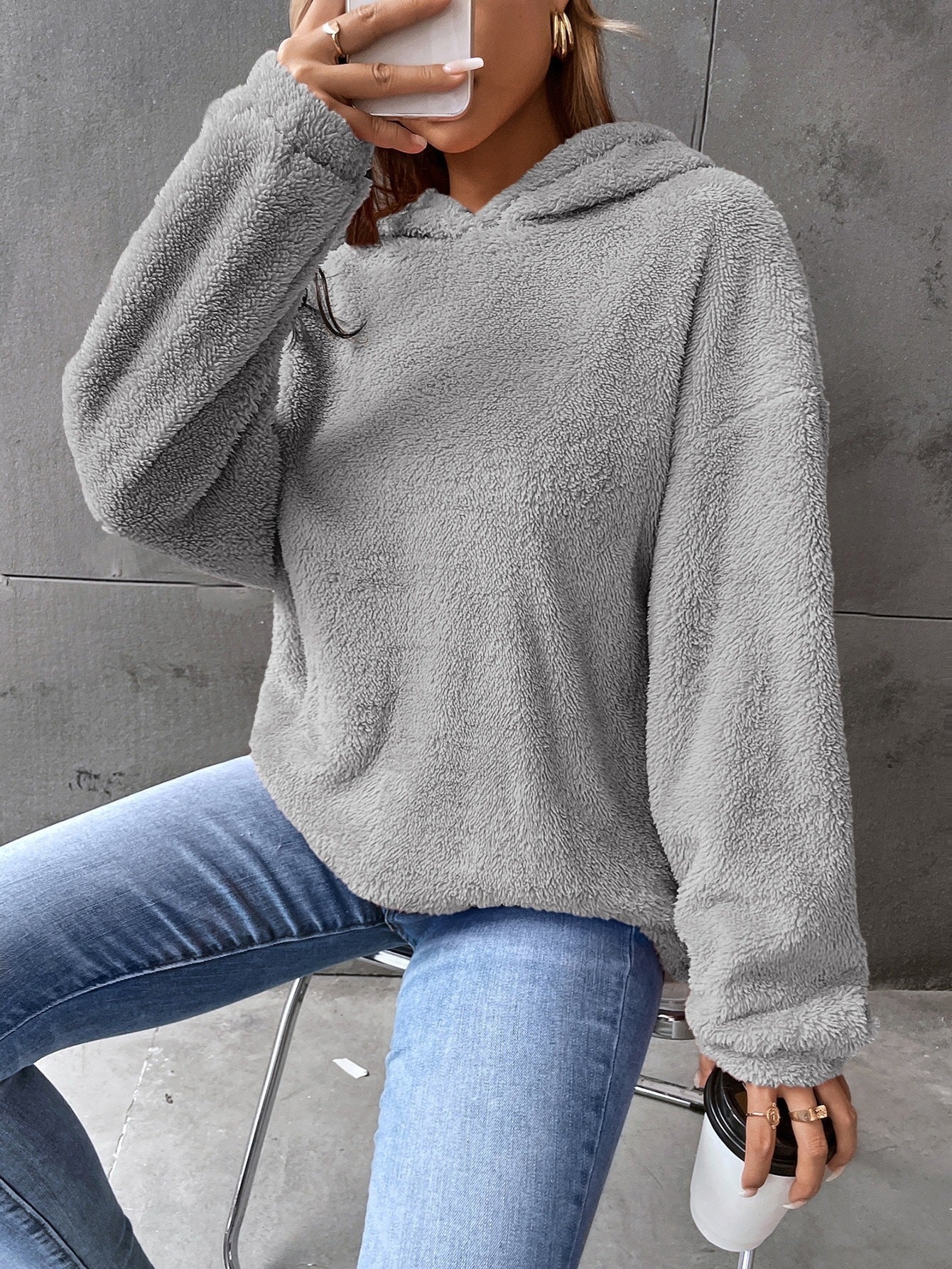 Femme portant un pull en polaire gris, tenant une tasse de café, assise sur une chaise. Mode décontractée, tendance automne-hiver, confort et style.