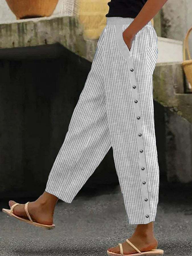 Pantalon rayé blanc à boutons latéraux, porté avec des sandales. Mode décontractée, tendance estivale, style urbain chic.