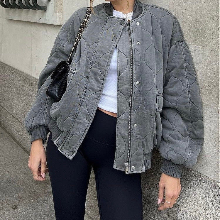 Femme portant un blouson matelassé gris, t-shirt blanc et leggings noirs, sac à main noir. Mode urbaine, tenue décontractée chic.