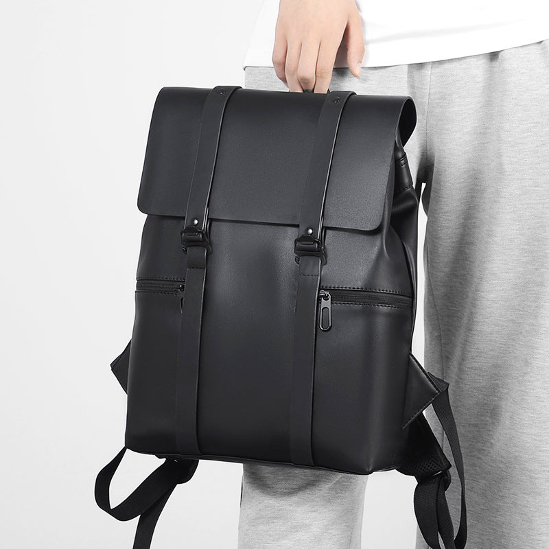 Sac à dos noir élégant en cuir synthétique, porté par une personne en pantalon gris. Design moderne avec poches zippées et bretelles ajustables.