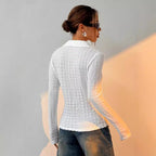 Femme de dos portant une chemise blanche texturée et un jean, coiffée d'un chignon, lunettes de soleil, éclairage doux. Mode féminine élégante.