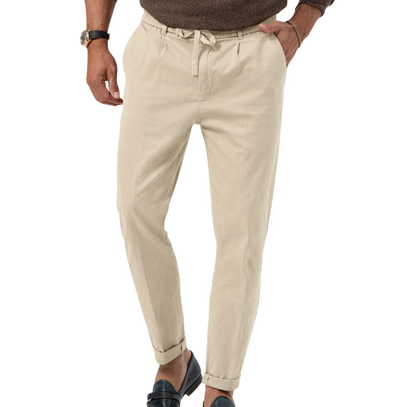 Pantalon beige homme en lin, coupe décontractée, avec ceinture à cordon, porté avec des mocassins noirs et un pull marron. Mode masculine élégante.