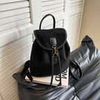 Sac à dos noir en cuir suédé sur canapé en cuir gris, posé sur un livre. Design élégant et moderne, idéal pour la mode urbaine et le quotidien.