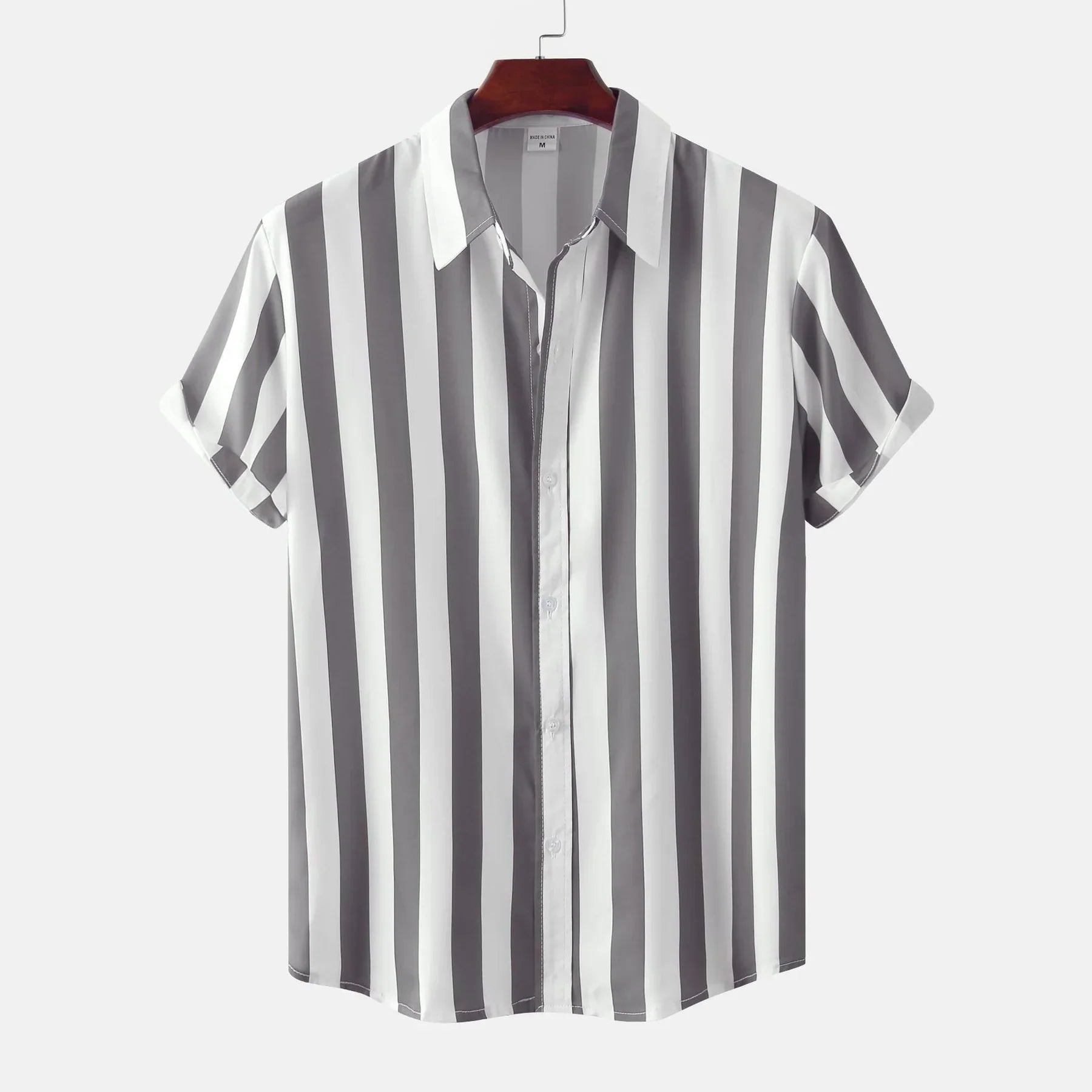 Chemise à manches courtes rayée noir et blanc, suspendue sur un cintre en bois, fond blanc. Mode homme, style décontracté, tendance été.