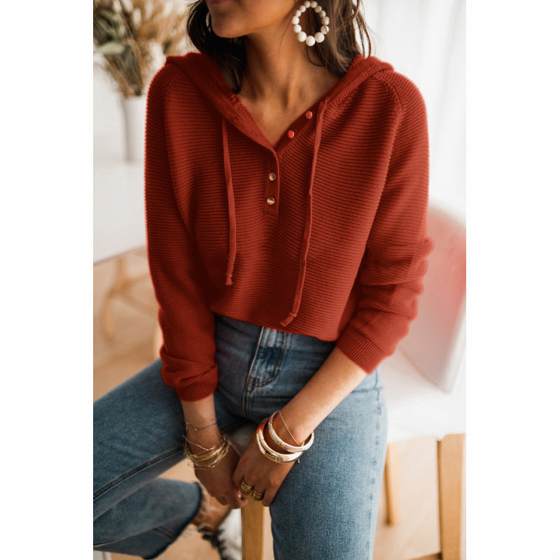 Femme portant un pull rouge à capuche avec boutons, jeans bleu, boucles d'oreilles pendantes et bracelets dorés. Mode décontractée automne-hiver.