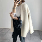 Femme en manteau blanc élégant, tenant un sac noir tressé, portant un t-shirt blanc et un pantalon noir. Mode chic et minimaliste.