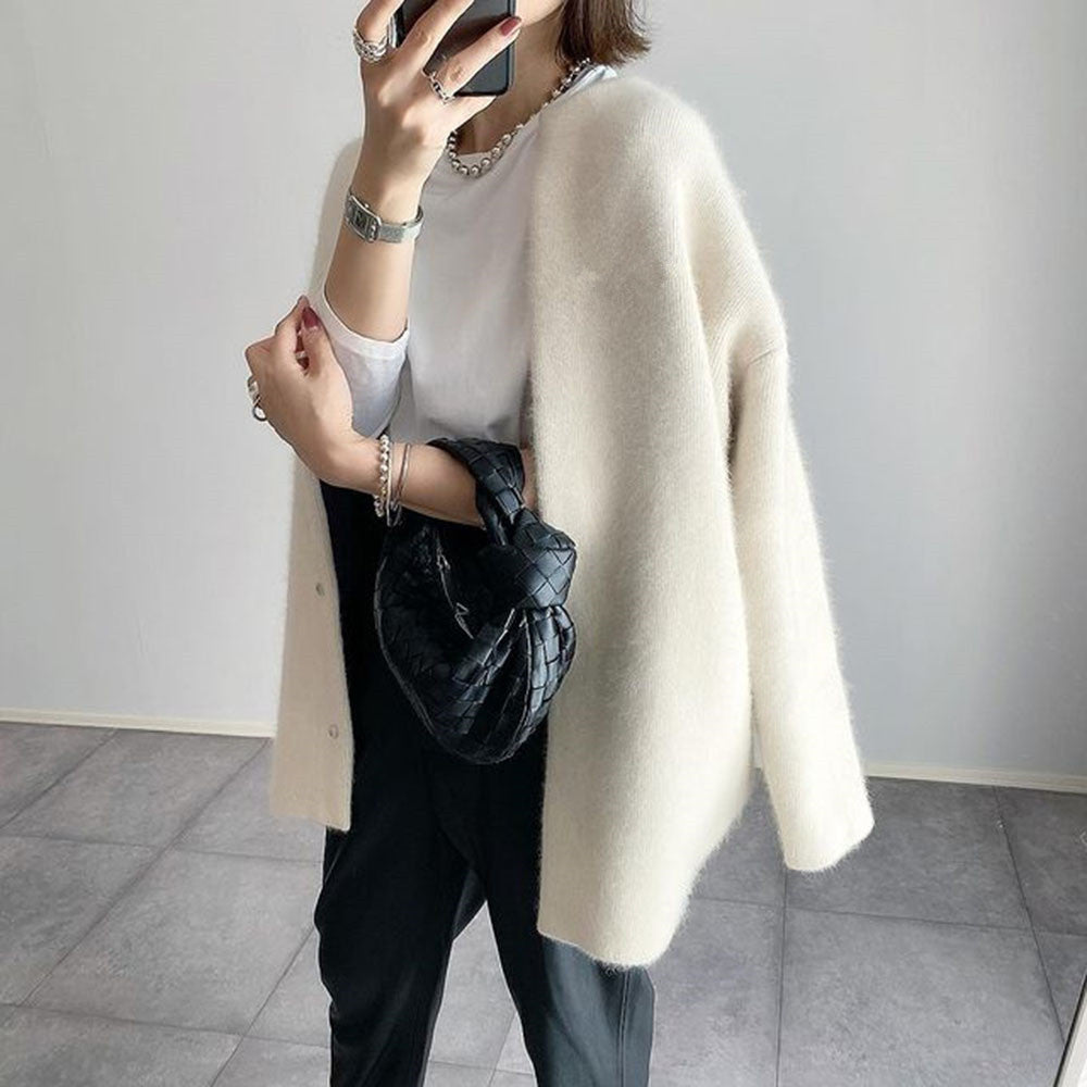 Femme en manteau blanc élégant, tenant un sac noir tressé, portant un t-shirt blanc et un pantalon noir. Mode chic et minimaliste.