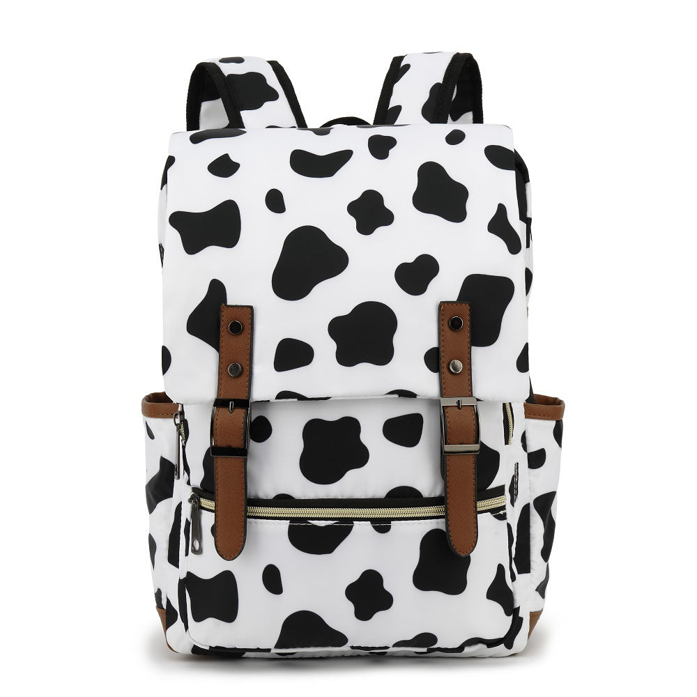 Sac à dos motif vache noir et blanc, design moderne, poches latérales, sangles marron, idéal pour école, voyage, mode tendance.