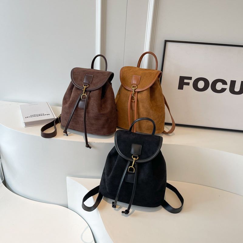 Trois sacs à dos en cuir suédé marron, beige et noir posés sur une table blanche, avec un cadre "FOCUS" en arrière-plan. Accessoires mode tendance.