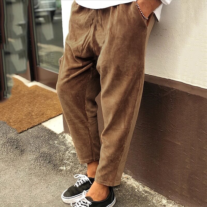 Pantalon en velours côtelé marron pour homme, coupe ample, style décontracté, porté avec des baskets noires et blanches, mode urbaine tendance.