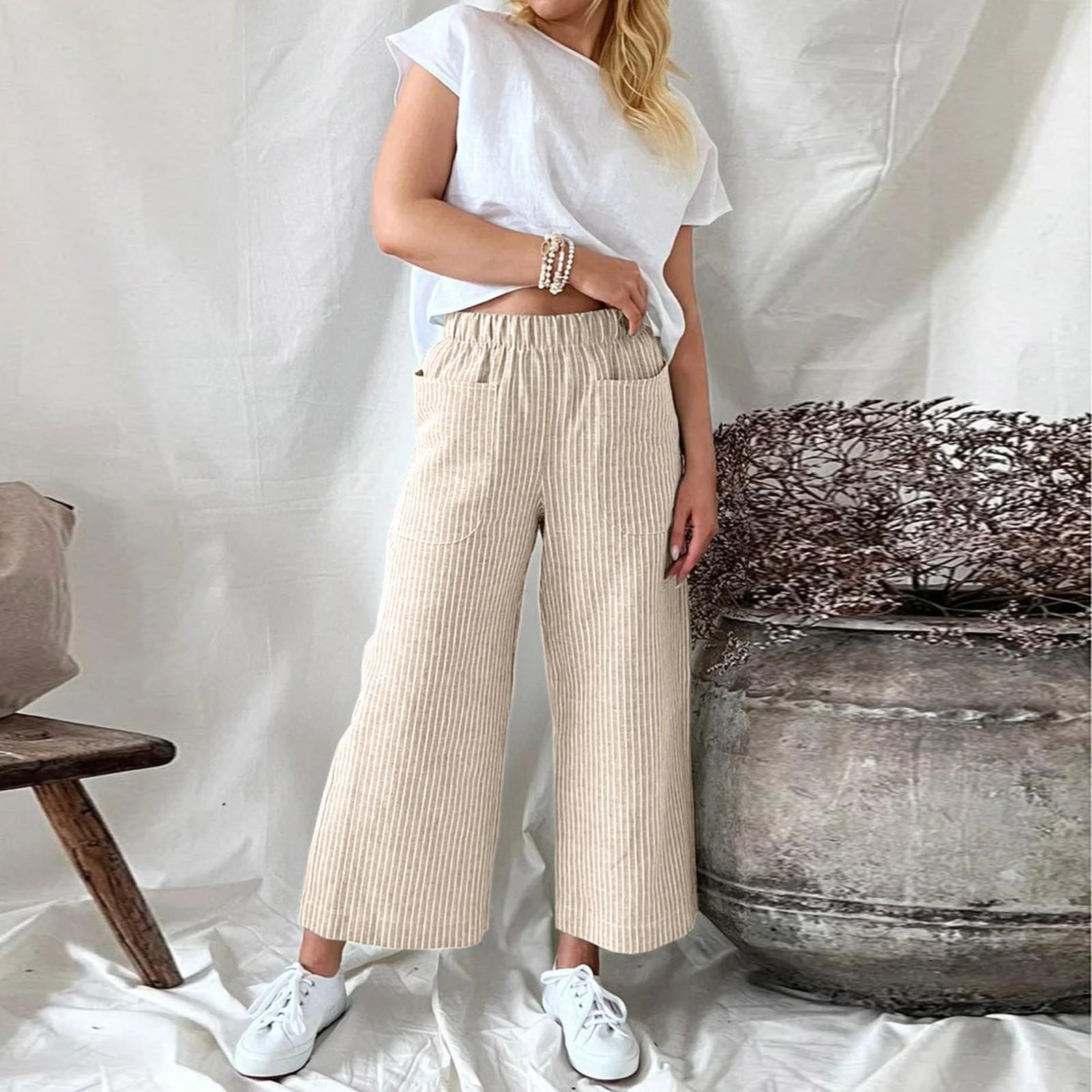 Femme portant un pantalon beige à rayures et un t-shirt blanc, posant près d'un pot en métal, style décontracté chic, mode féminine tendance.