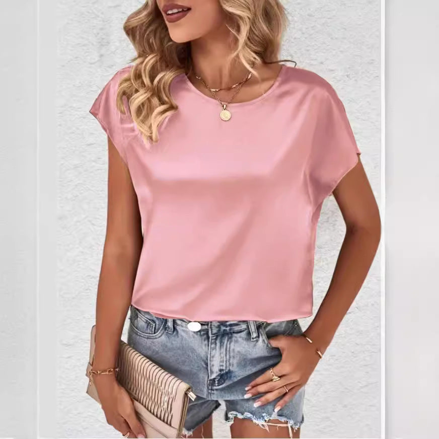 Femme en haut rose satiné, cheveux blonds bouclés, portant un short en jean et un sac à main beige. Mode estivale élégante et décontractée.