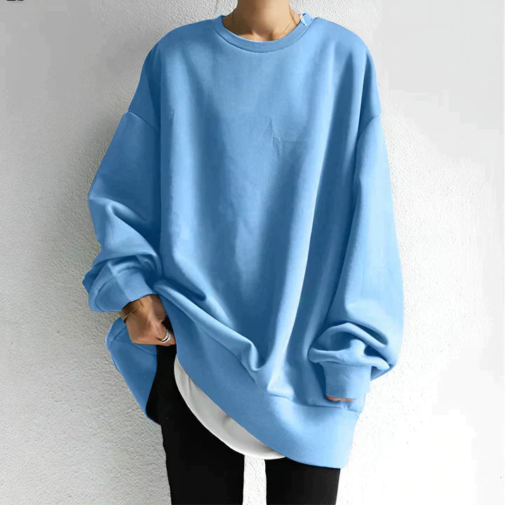 Personne portant un sweat-shirt bleu oversize, manches longues, sur un t-shirt blanc. Mode décontractée, tendance streetwear, style confortable.