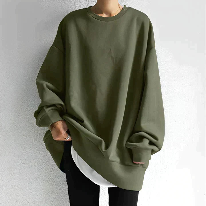 Personne portant un sweat-shirt oversize vert kaki, manches longues, sur un t-shirt blanc, avec un fond blanc. Mode décontractée, tendance automne.