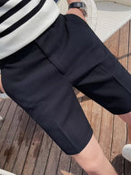 Short en tissu texturé noir pour homme, style décontracté, porté en extérieur sur terrasse en bois. Mode masculine estivale, confort et élégance.