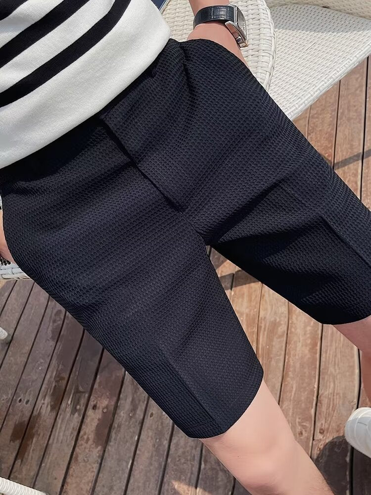 Short en tissu texturé noir pour homme, style décontracté, porté en extérieur sur terrasse en bois. Mode masculine estivale, confort et élégance.