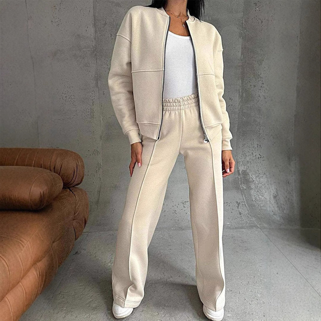 Femme portant un ensemble de survêtement beige, composé d'une veste zippée et d'un pantalon ample, posant dans un intérieur moderne.