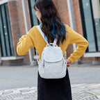 Femme de dos portant un sac à dos blanc, vêtue d'un pull jaune et jupe noire, marchant en ville. Mode urbaine, style décontracté, accessoires tendance.