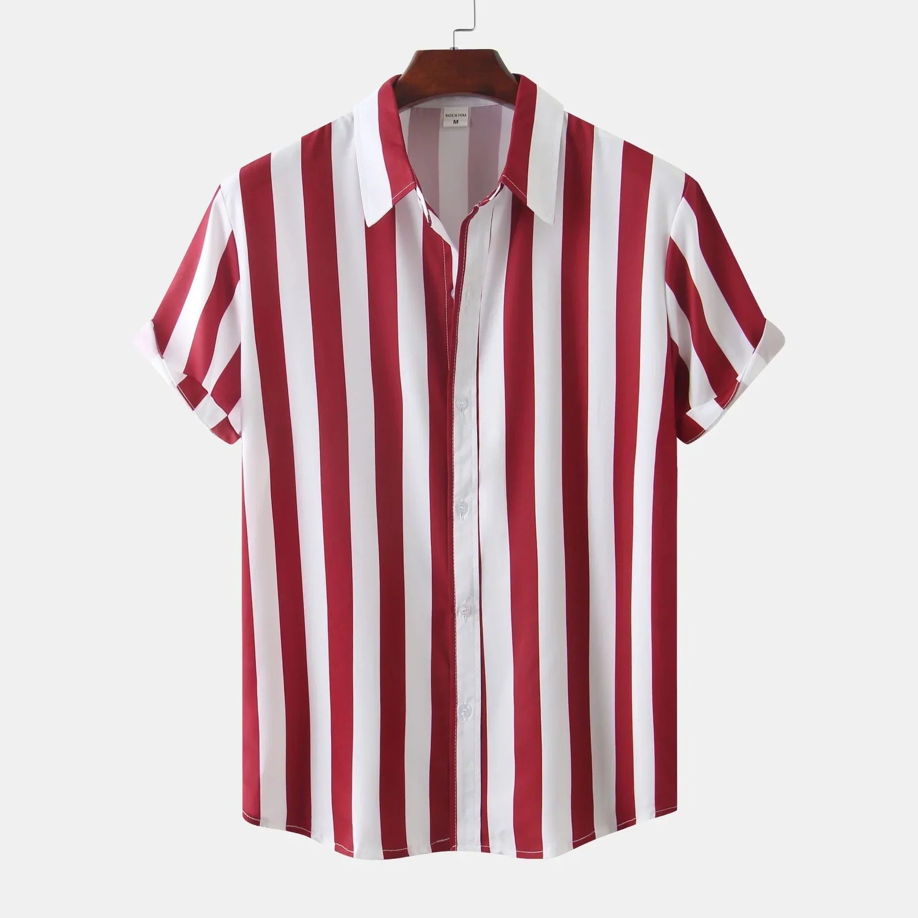 Chemise à manches courtes rayée rouge et blanche, col classique, style décontracté, suspendue sur un cintre en bois, fond blanc.