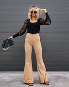 Femme élégante en tenue chic: pull noir à manches transparentes, pantalon beige évasé, lunettes de soleil, sac noir. Mode tendance automne.