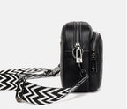 Sac bandoulière en cuir noir avec fermeture éclair argentée et sangle à motif zigzag noir et blanc, design moderne et élégant.