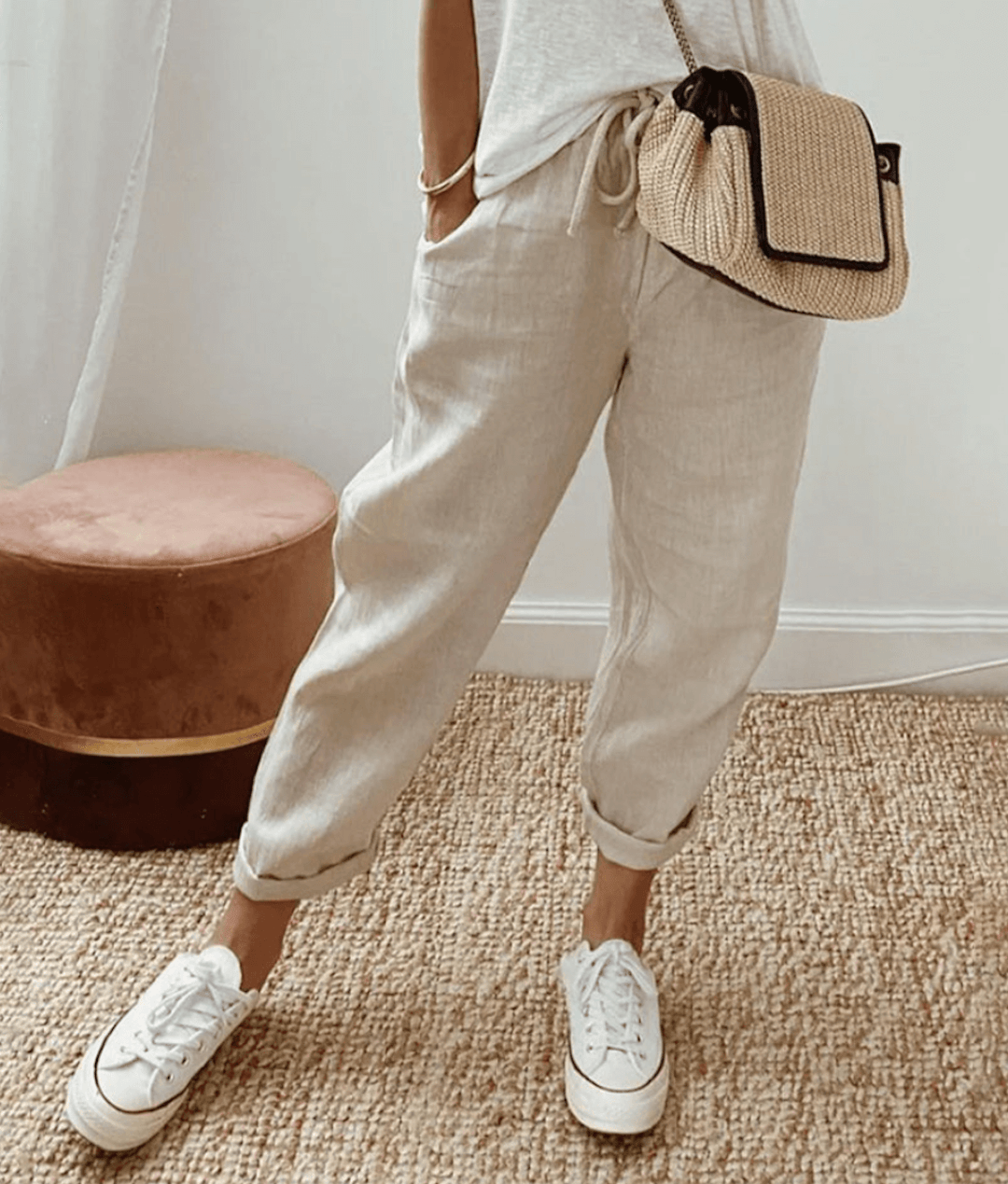 Pantalon en lin beige, décontracté, avec cordon de serrage, porté avec des baskets blanches et un sac en paille, style estival chic et confortable.