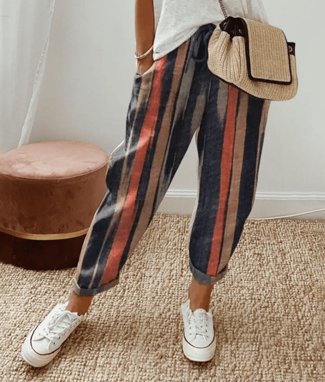 Pantalon rayé multicolore femme, style décontracté, avec sac à main en paille et baskets blanches. Mode tendance, tenue confortable.