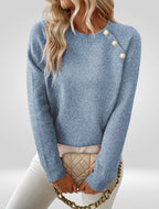 Femme portant un pull bleu avec boutons décoratifs, tenant un sac à main matelassé beige à chaîne dorée. Mode automne, style élégant et chic.