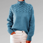Pull en laine bleu avec motif torsadé, col montant, manches longues, porté avec un pantalon blanc. Mode hiver, style décontracté et élégant.