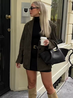 Femme élégante en manteau marron, robe noire, bottes beiges, lunettes de soleil, tenant un café devant une porte. Mode automne chic, style urbain.