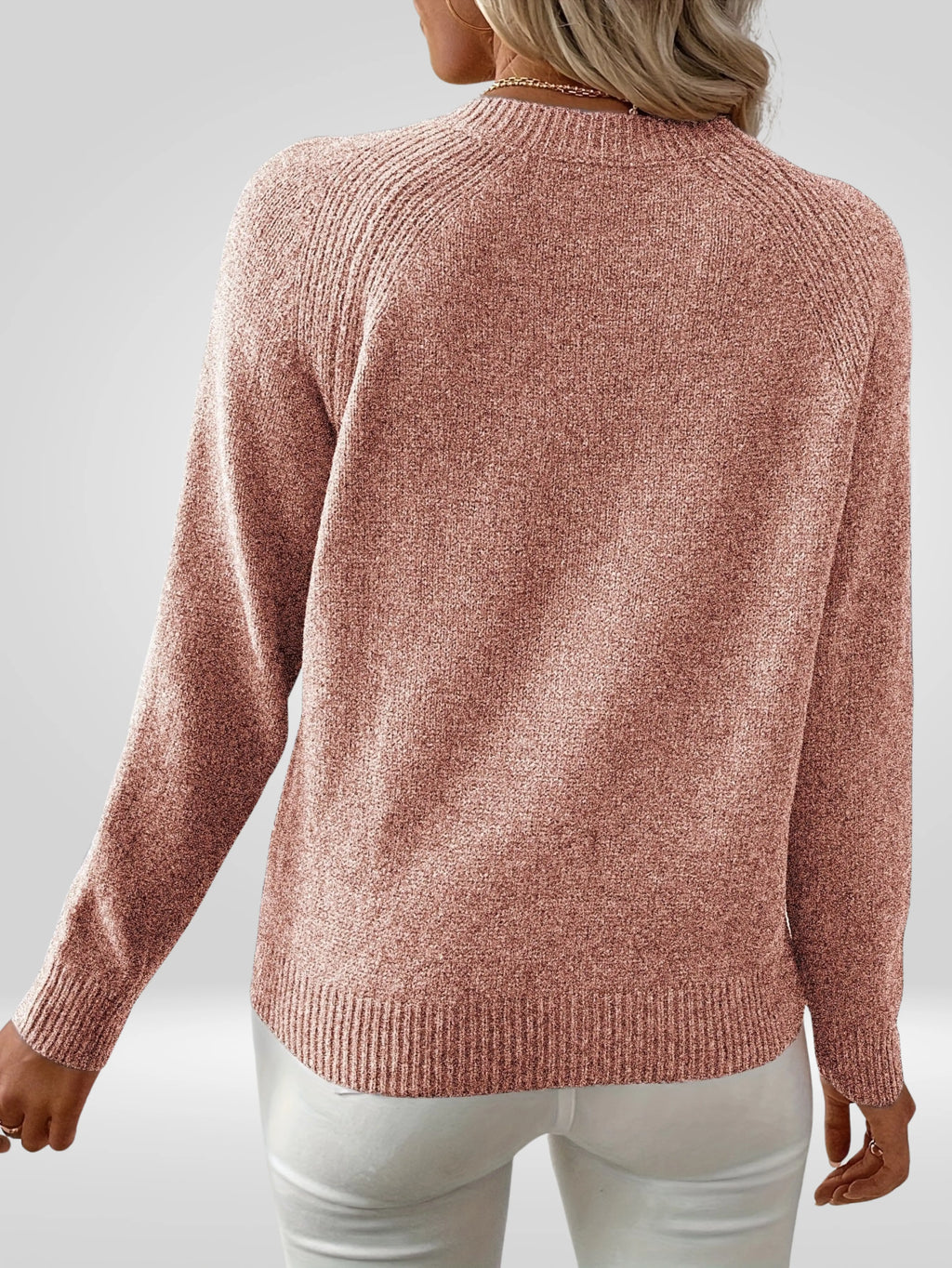 Femme portant un pull rose en tricot à manches longues, vue de dos, sur fond gris. Mode automne-hiver, style décontracté et élégant.