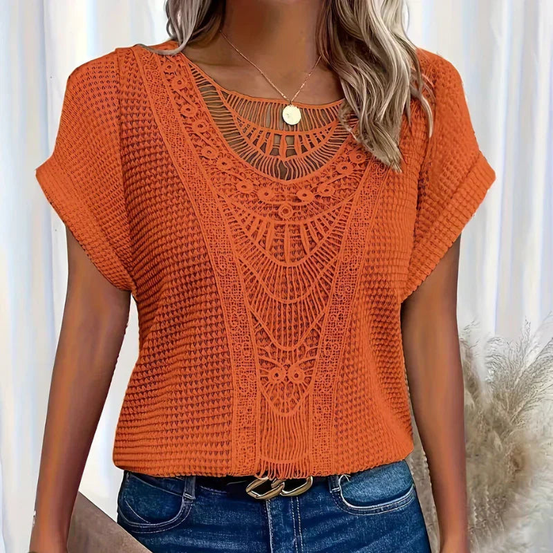 Femme portant un haut en crochet orange, manches courtes, avec un motif ajouré complexe, associé à un jean bleu. Mode féminine tendance.