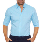 Homme portant une chemise bleue à manches retroussées, col classique, boutons blancs, style décontracté. Mode masculine élégante et moderne.