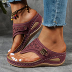 Sandales violettes pour femme avec détails perforés, portées avec un jean déchiré et un bracelet de cheville coloré. Mode estivale, chaussures confortables.