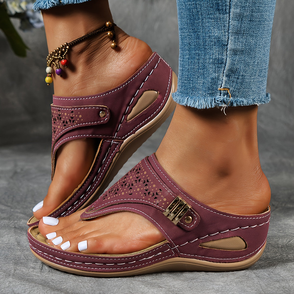Sandales violettes pour femme avec détails perforés, portées avec un jean déchiré et un bracelet de cheville coloré. Mode estivale, chaussures confortables.