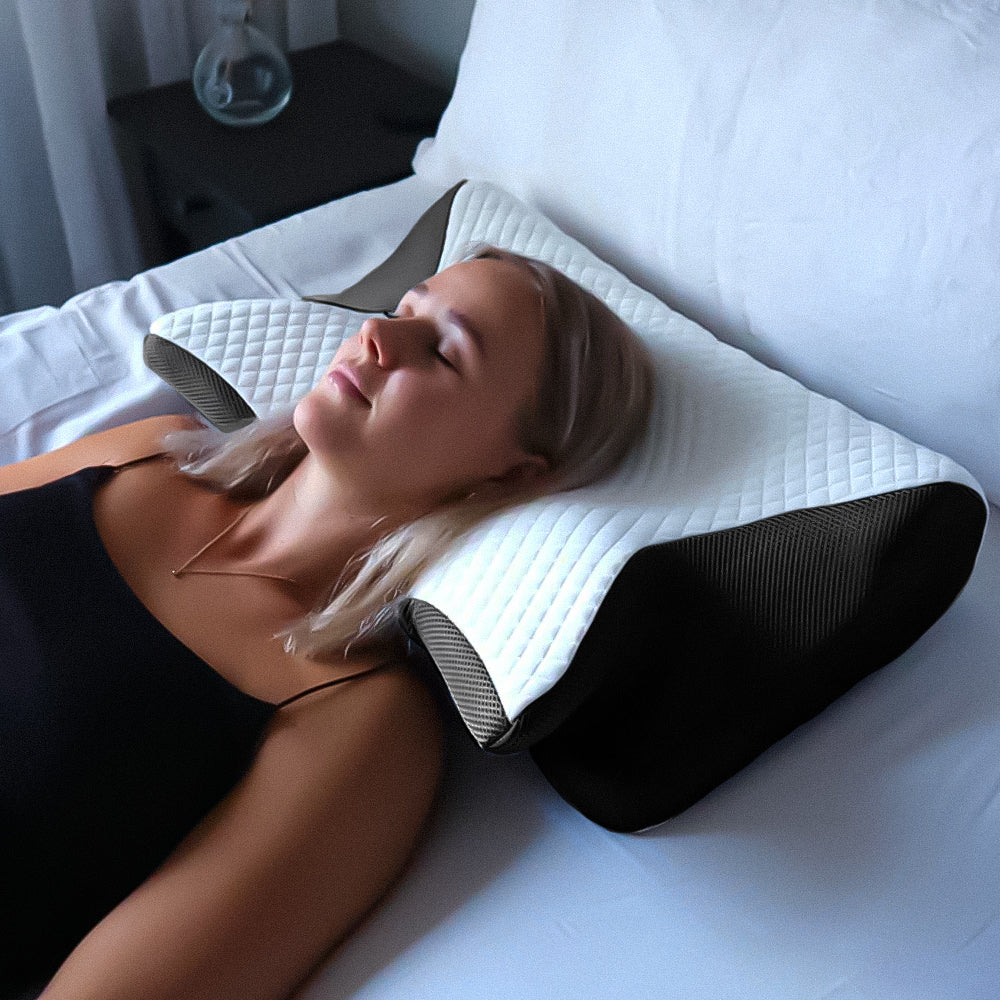 Femme dormant sur un oreiller ergonomique en mousse à mémoire de forme, offrant un soutien optimal pour le cou et la tête, sur un lit blanc.