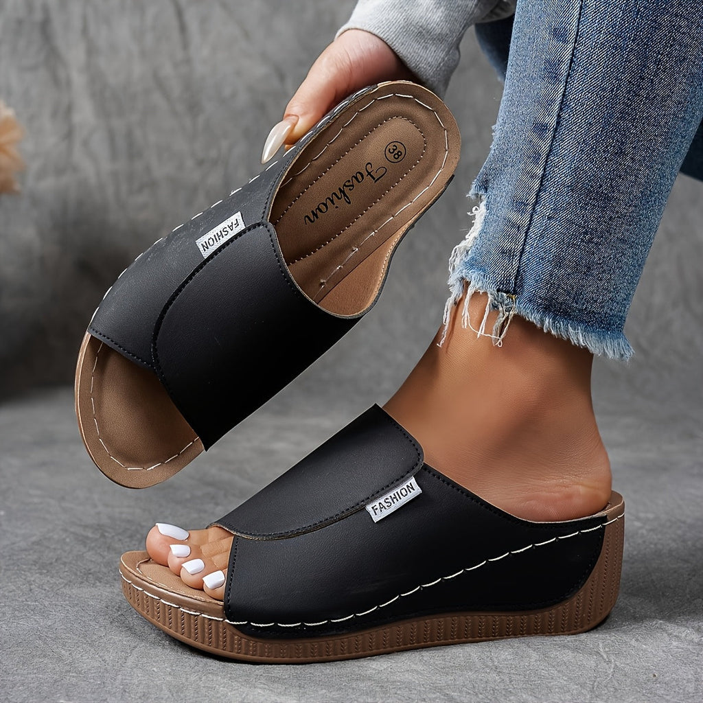 Sandales noires en cuir synthétique pour femmes, avec semelle compensée marron et étiquette "Fashion", portées avec un jean décontracté.
